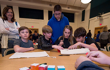 five students and a parent gathered around a table working on a problem