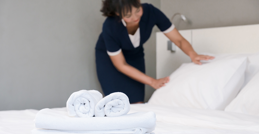 Young maid making bed in a room, focus of clean towels