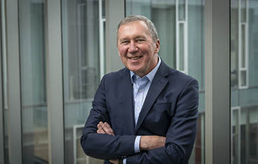 Tom Mitchell stands in front of glass windows at Gates Center on CMU's campus