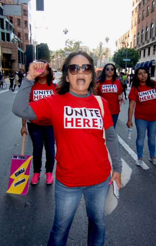 Woman wearing red UNITE HERE shirt shouts with fist raised