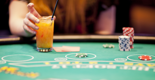 Hand holding a large cocktail in a glass on a casino card table